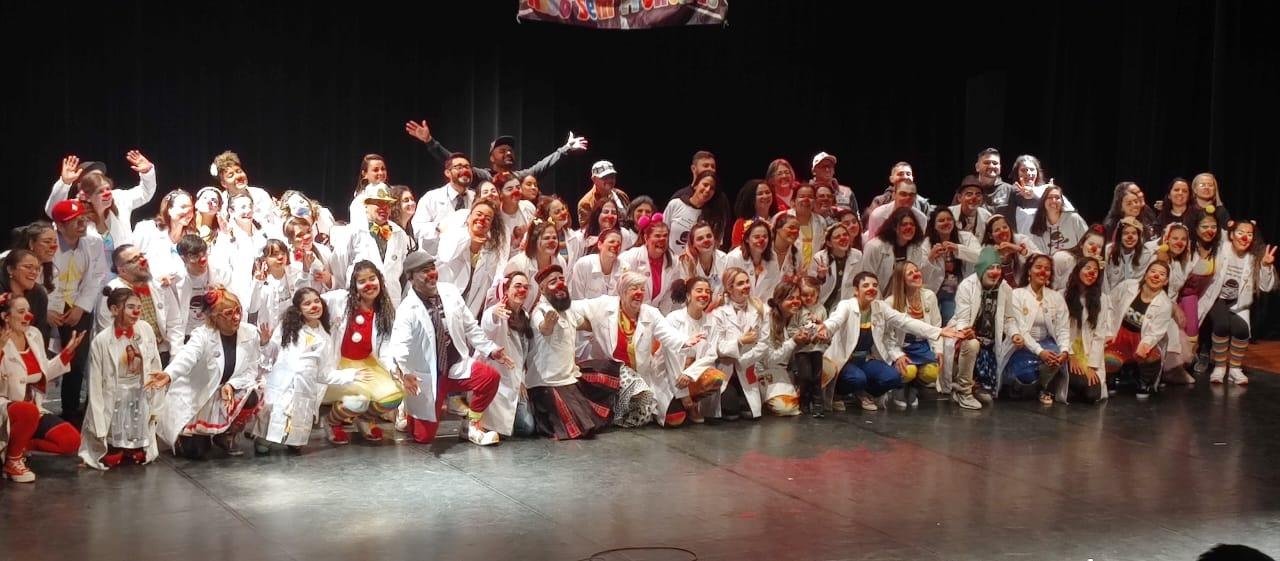 Formatura de 48 novos Drs. Risologistas da Riso Sem Fronteiras em 2024 — toda a turma reunida no palco com jaleco branco e nariz vermelho