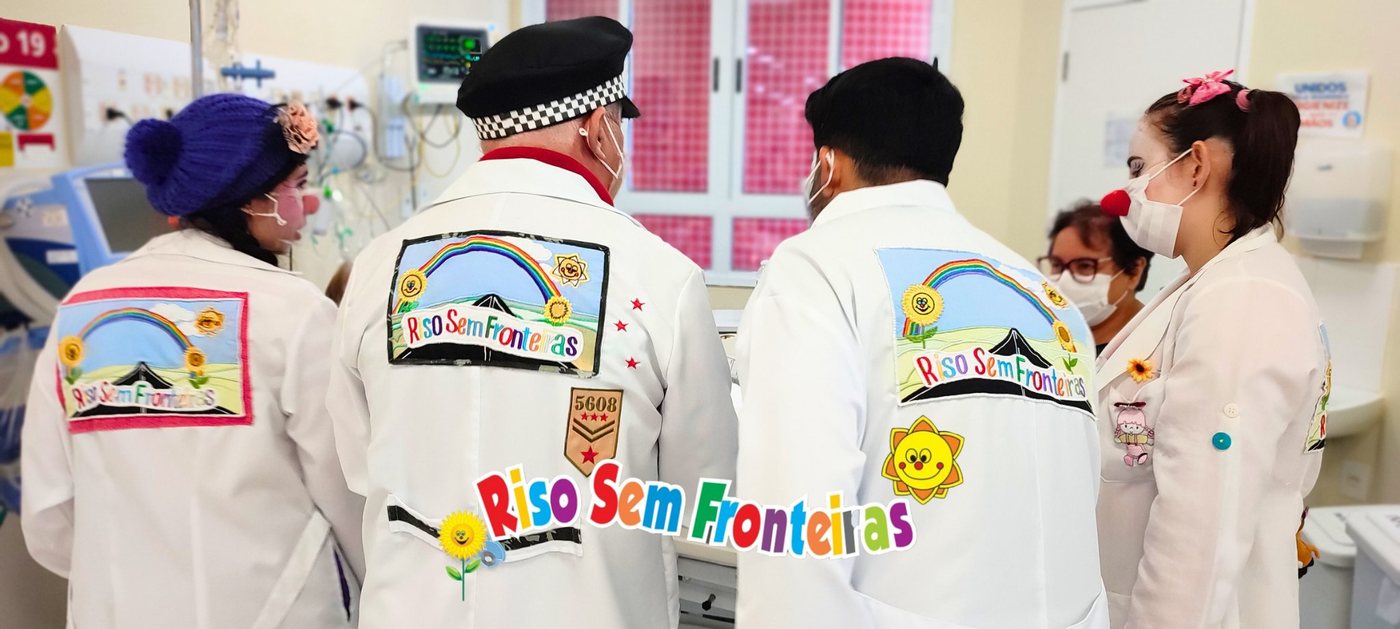 Voluntários com jalecos da Riso Sem Fronteiras em ambiente hospitalar — logo bordado em destaque